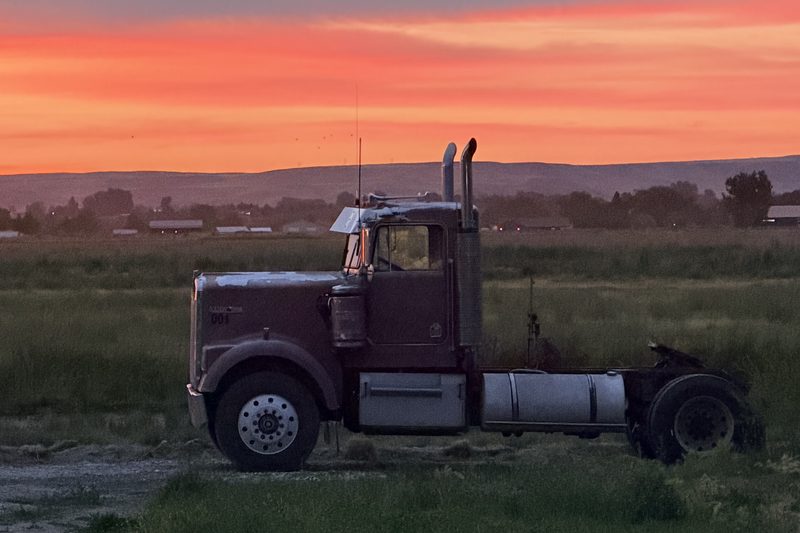 A long-nose Kenworth conventional parked in a field at sunset